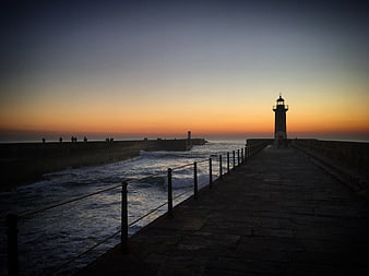 Silhouette of Lighthouse on Pier at Sunset with Crashing Waves