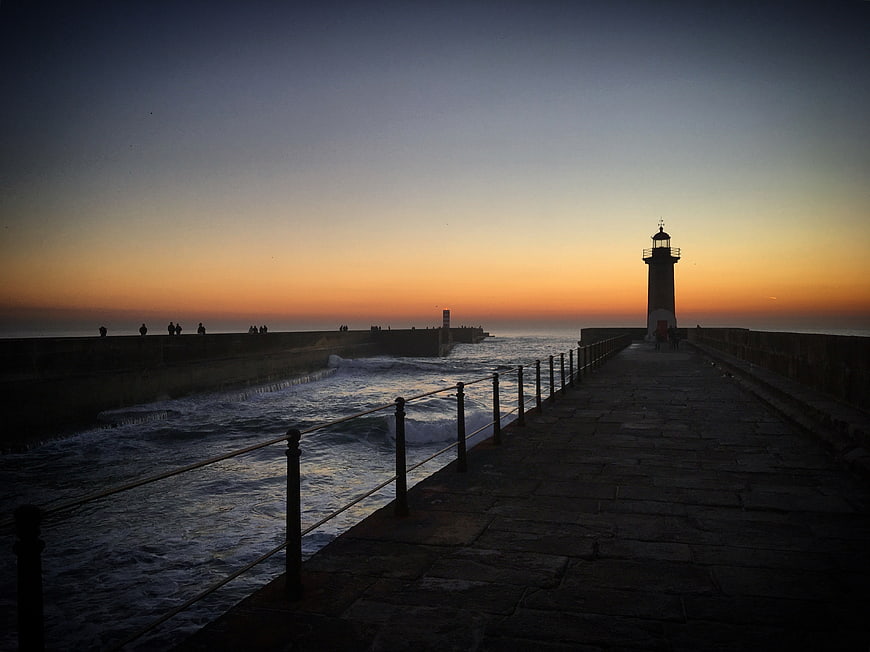 Silhouette of Lighthouse on Pier at Sunset with Crashing Waves