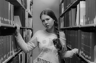 Young woman with braid browsing books in library aisle