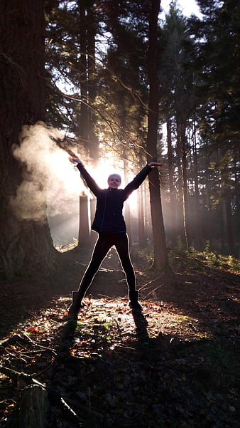 Woman with arms raised in sunlit forest with breath vapor