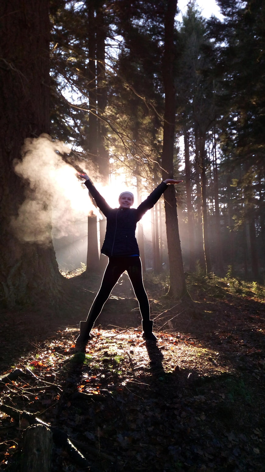Woman with arms raised in sunlit forest with breath vapor