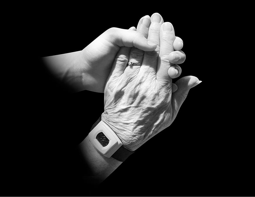 Young hand holding elderly hand with medical wristband in black and white