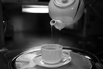 Black and white teapot pouring tea into cup on tray