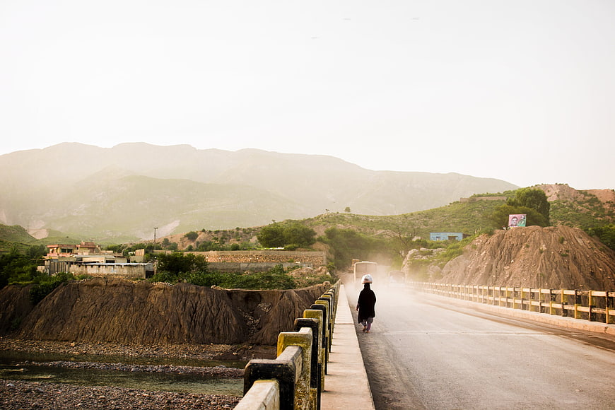Lone figure walking on a dusty bridge in a rural mountain landscape