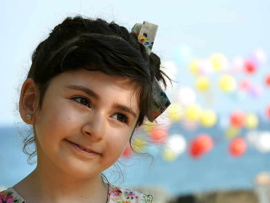 Close-up portrait of a smiling young girl with a bow and balloons