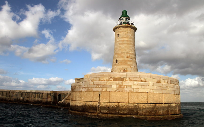 Historic stone lighthouse on a breakwater under cloudy sky