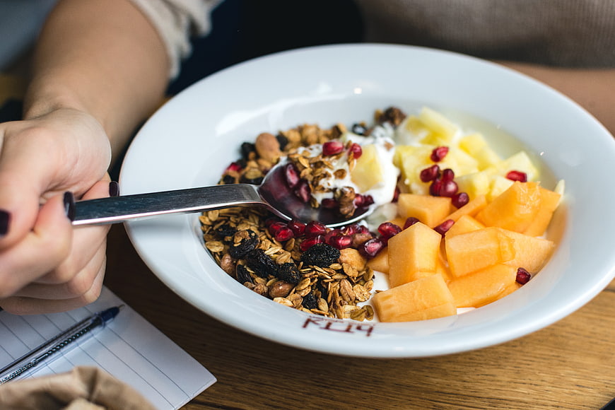 Close-up of hand eating granola bowl with fresh fruit