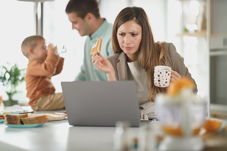 Stressed mother working on laptop during family breakfast