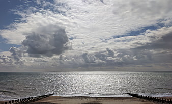 Dramatic Cloudy Sky Over Sparkling Sea with Wooden Groynes