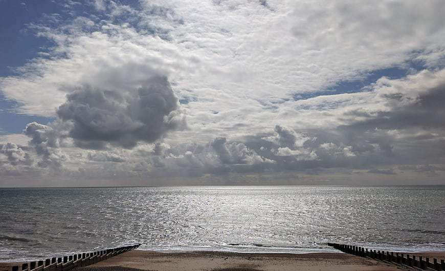 Dramatic Cloudy Sky Over Sparkling Sea with Wooden Groynes