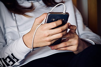 Close-up of hands holding smartphone with white earphones