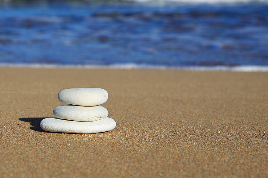 Stacked white stones on sandy beach with ocean background