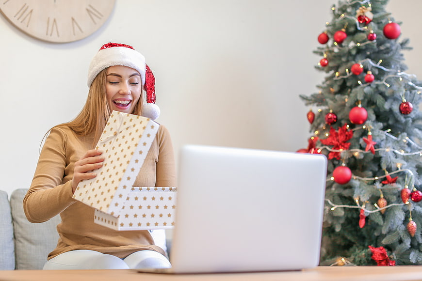 Happy woman opening Christmas gift online with laptop