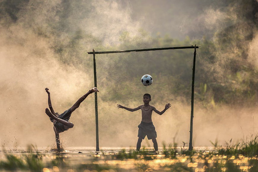 Boys Playing Soccer in Muddy Field at Sunset