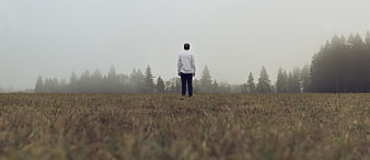 Man standing alone in foggy field looking at forest