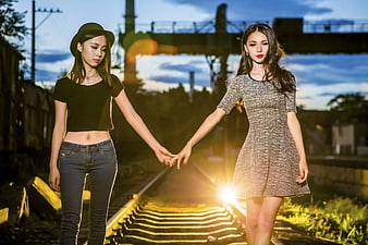 Two Women Holding Hands Walking on Train Tracks at Sunset