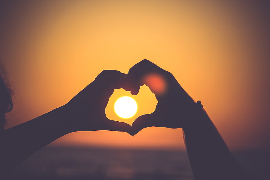 Silhouette of Hands Making Heart Shape Around Sunset Sun
