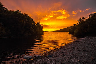 Dramatic Orange Sunset Over River with Silhouetted Trees