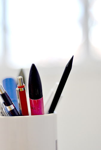 Colorful pens in a white cup on a desk