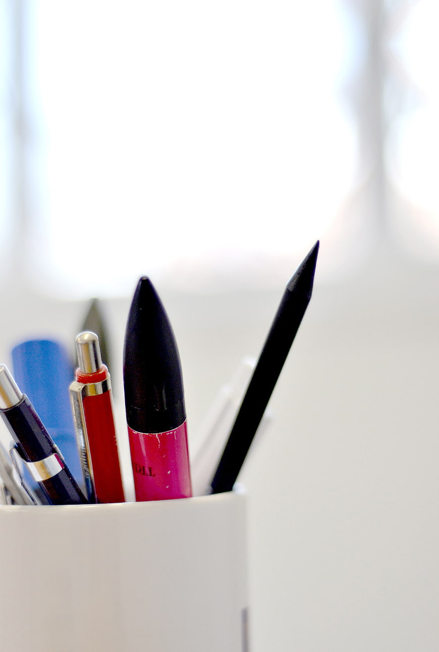 Colorful pens in a white cup on a desk