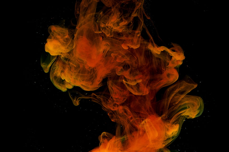 Vibrant orange and yellow ink swirling in dark water abstract background