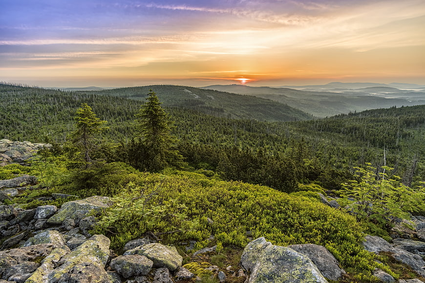Sunset over rolling forested mountains with rocky foreground