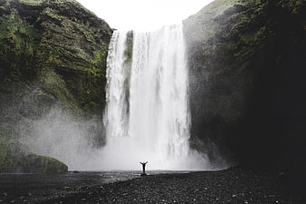 Person with open arms standing before a massive waterfall in Iceland