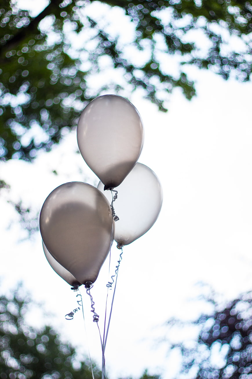 Silver balloons floating against a bright sky with blurred green tree foliage
