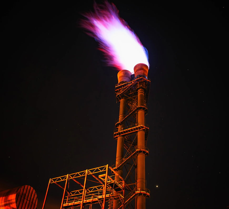 Gas Flare Tower Burning at Night with Purple Flame