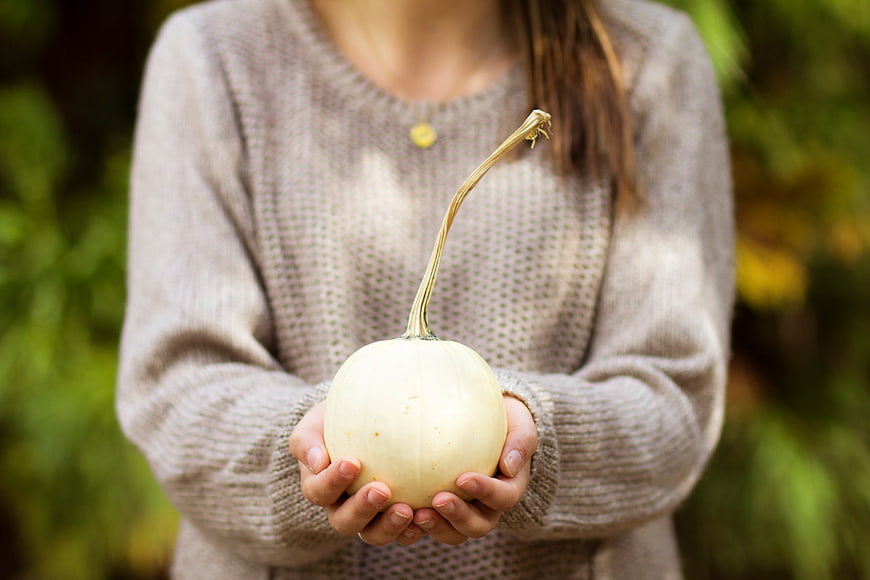 Woman holding white pumpkin in cozy knit sweater