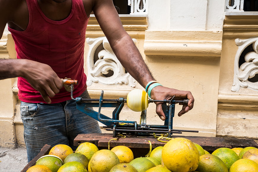 Man peeling yellow oranges with manual crank machine in Cuba