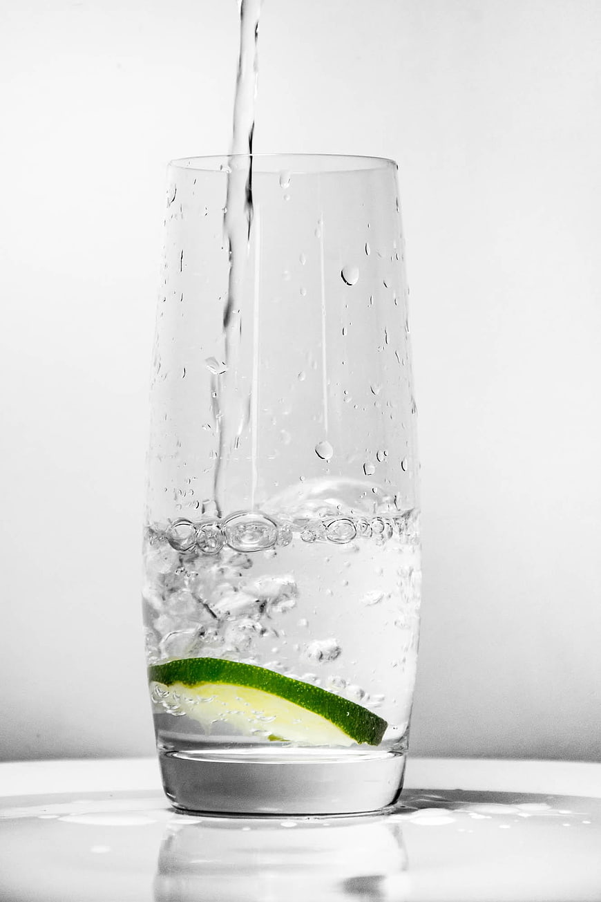 Refreshing glass of water with lime slice and pouring stream