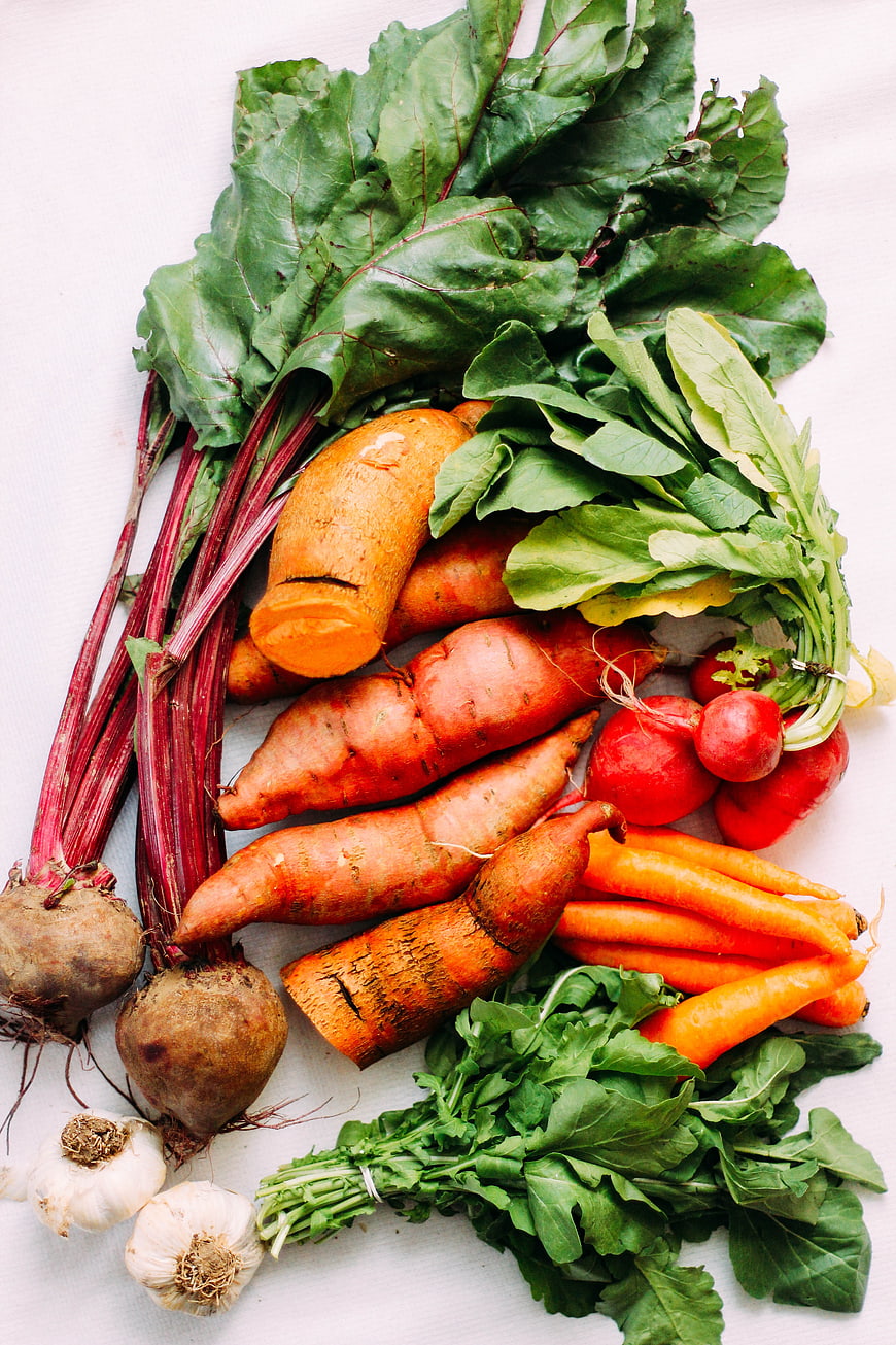 Fresh organic root vegetables and greens on white background