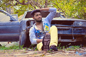 Young man sitting in front of a wrecked car outdoors