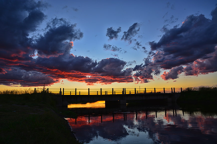 Dramatic sunset over a bridge with vibrant red clouds and water reflections