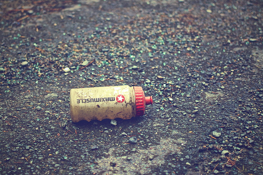 Dirty sports water bottle lying on gravel ground