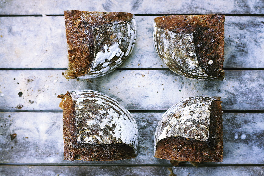 Four rustic sourdough bread loaves on weathered wooden planks