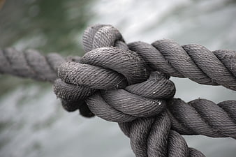 Close-up of thick gray rope knot with blurred water background
