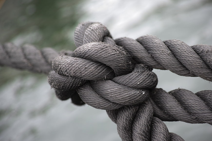 Close-up of thick gray rope knot with blurred water background