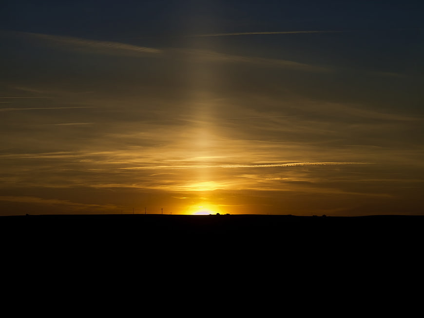 Golden sunset over dark silhouette landscape with sun rays