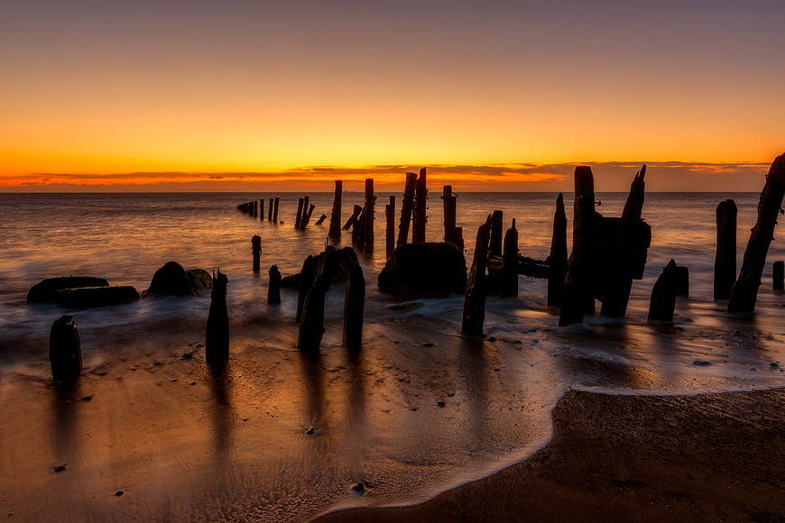 Silhouetted Wooden Pilings on Sandy Beach at Golden Sunset