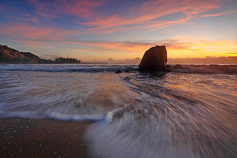 Long exposure beach sunset with smooth flowing waves and dramatic rock formation