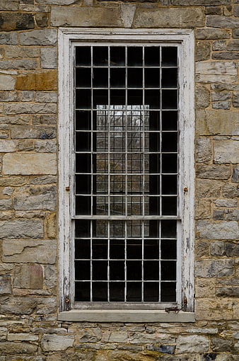 Old white grid window on textured stone wall exterior
