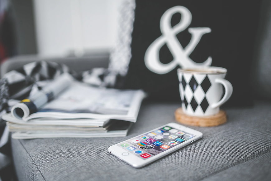 White smartphone on gray couch with coffee cup and magazines