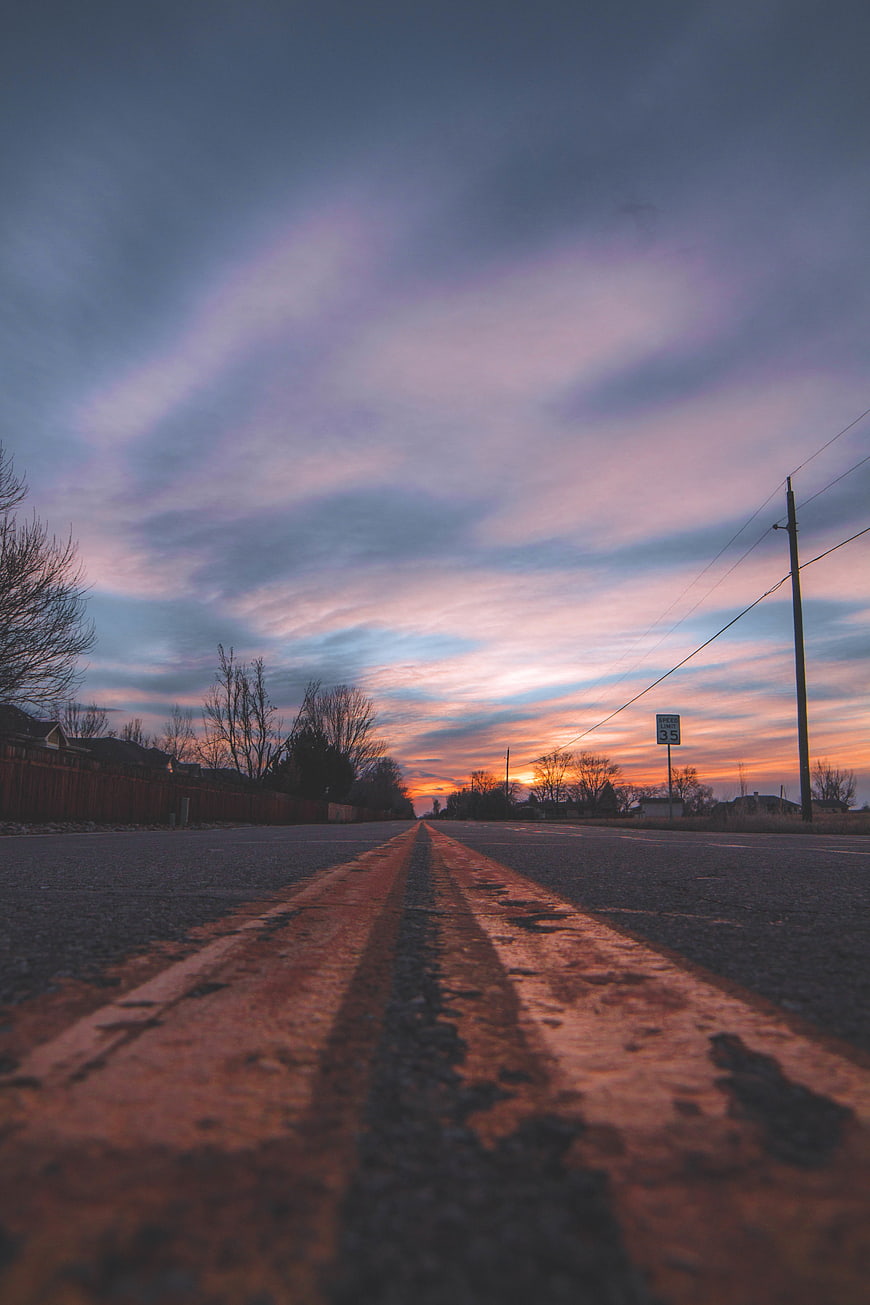 Low angle view of empty road with double yellow lines at sunset