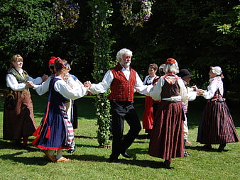 Group of people in traditional folk costumes dancing outdoors in a garden