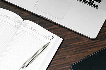 Open planner, pen, and laptop on wooden desk workspace