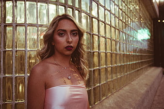 Stylish blonde woman in pink dress against glass block wall