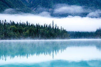 Misty turquoise lake with forest reflection and foggy mountains