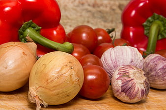 Fresh red peppers, onions, tomatoes, and garlic on wooden board
